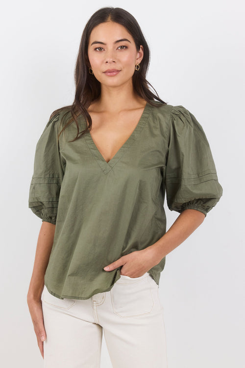 Woman wearing an olive green blouse with puff sleeves on a white background