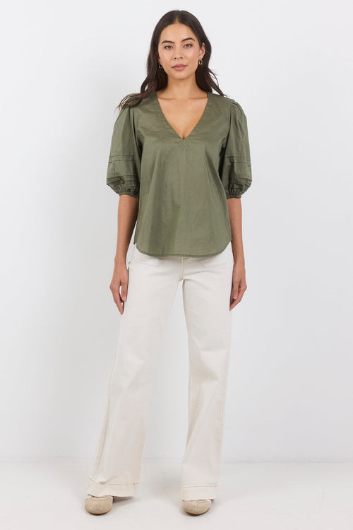 Woman wearing a green blouse and white pants on a white background
