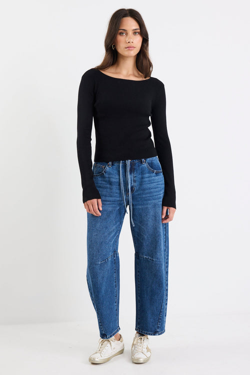 Woman wearing a black long-sleeve top and blue jeans on a white background