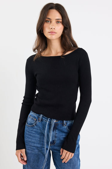 Woman wearing a black long-sleeve top and blue jeans on a white background
