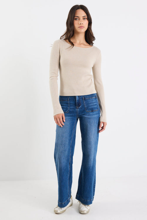 Woman wearing a beige sweater and blue jeans on a white background