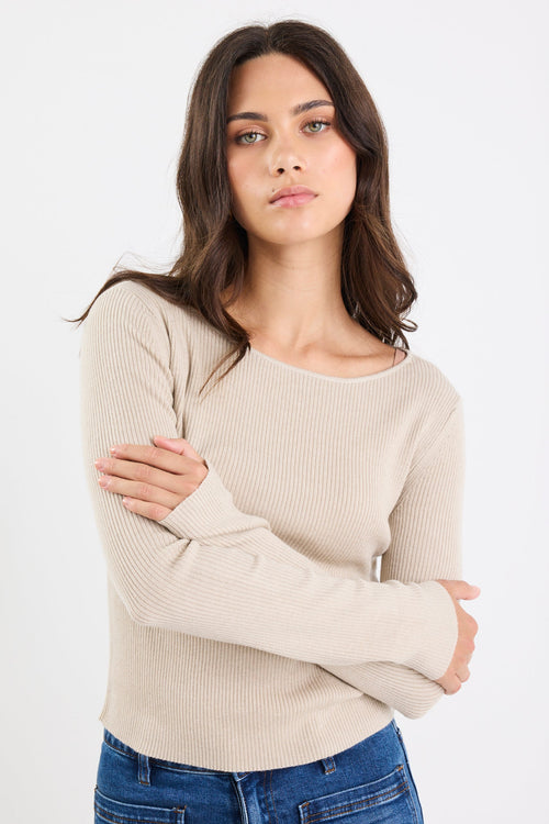 Woman wearing a beige sweater and blue jeans against a white background
