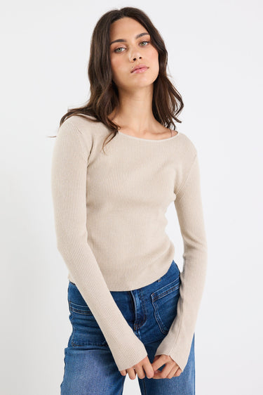 Woman wearing a beige sweater and blue jeans on a white background