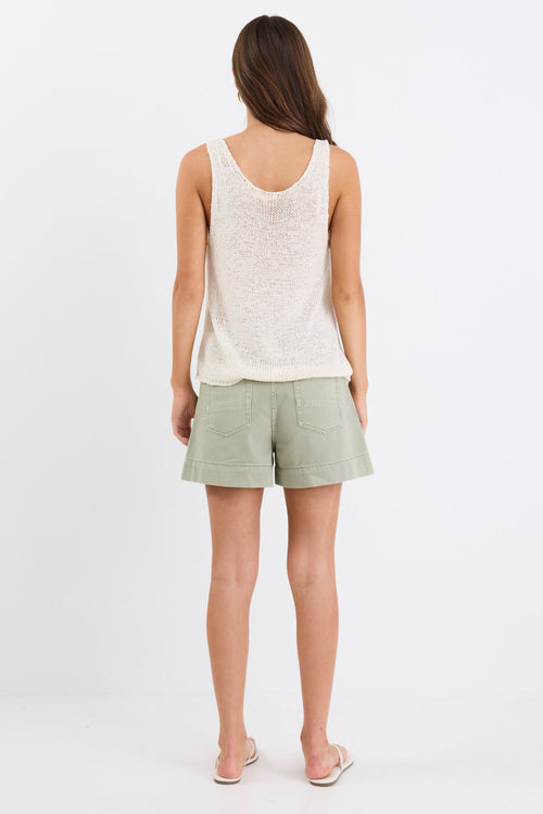 Woman wearing khaki high-rise denim shorts with a relaxed leg and zip closure, paired with a cream knitted tank and sandals, standing against a white background.