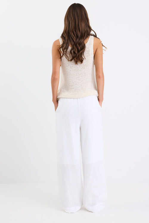Woman wearing white linen wide leg pants with an elastic waistband, paired with a cream knit tank and sandals, standing against a white background.