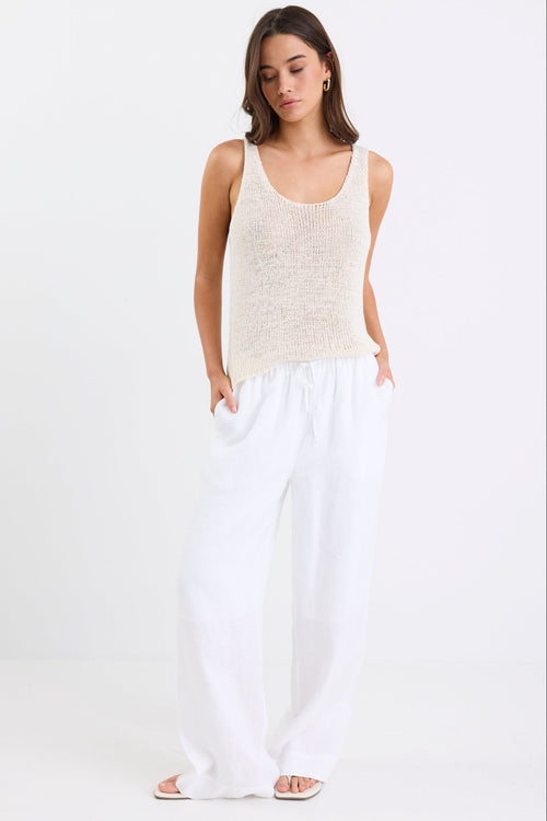 Woman wearing white linen wide leg pants with an elastic waistband, paired with a cream knit tank and sandals, standing against a white background.