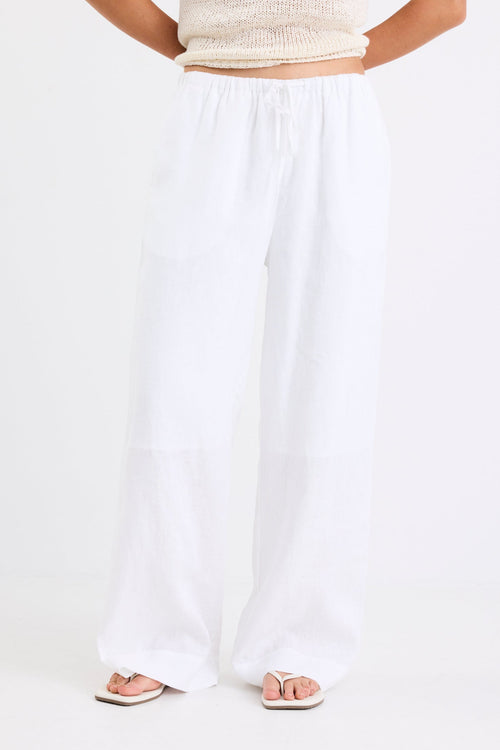 Woman wearing white linen wide leg pants with an elastic waistband, paired with a cream knit tank and sandals, standing against a white background.