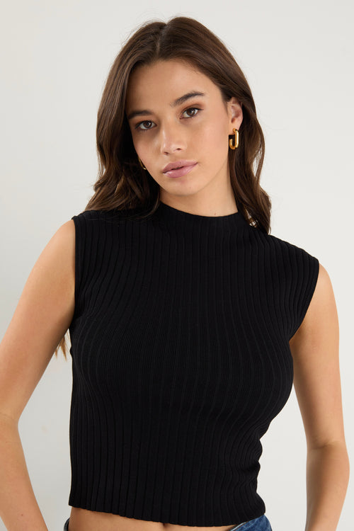 Model wears a black rib knit top with dark blue jeans