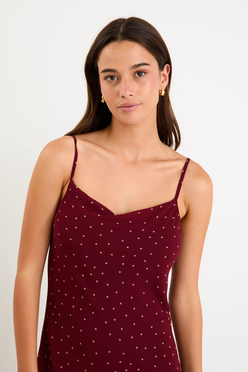 Model wearing a burgundy polka dot strappy maxi dress with a bias-cut silhouette and a flowy skirt