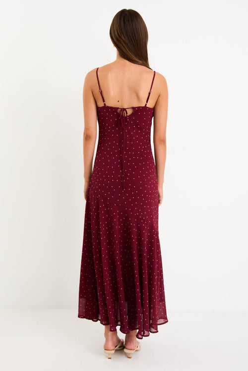 Model wearing a burgundy polka dot strappy maxi dress with a bias-cut silhouette and a flowy skirt
