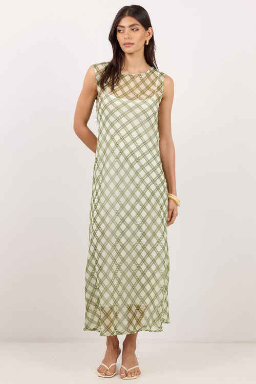 A woman modeling a sleeveless midi dress with a sage green and beige gingham pattern, standing against a plain off-white studio background.