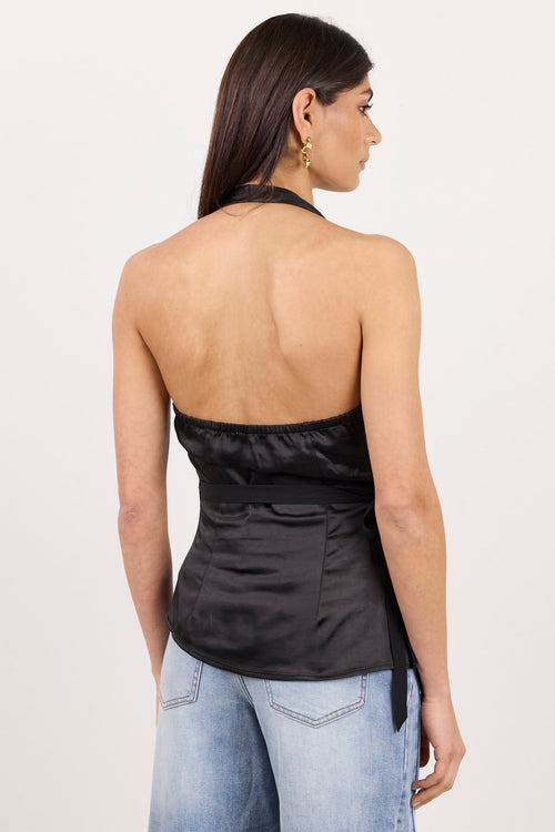 A woman shown from the back wearing a black satin halter top and light blue jeans, standing against a plain off-white studio background.