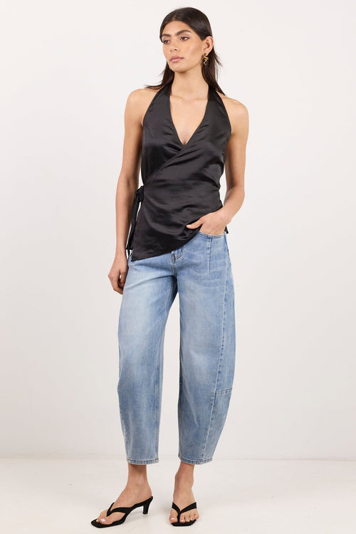A woman modeling a black satin halter top and light-wash cropped jeans against a plain white studio background.
