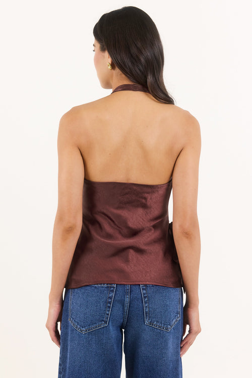 A woman shown from the back wearing a dark brown satin halter top and blue jeans against a plain white background.