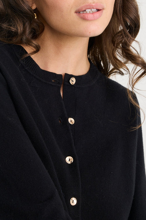 Woman wearing a black cardigan with gold buttons against a white background