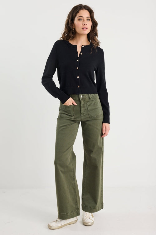 Woman wearing a black cardigan and green pants on a white background
