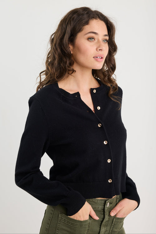 Woman wearing a black cardigan with gold buttons on a white background