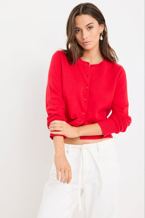 Woman wearing a cherry red crewneck cardigan with long sleeves and button-front closure, styled with denim jeans.