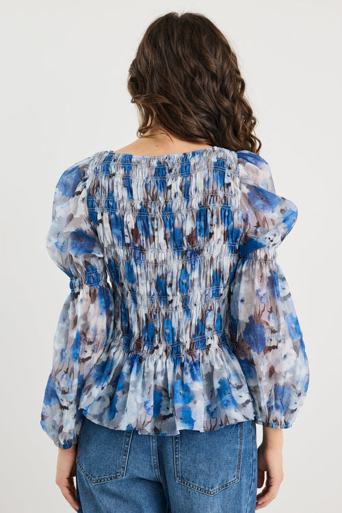 Woman wearing a blue and white patterned blouse with blue jeans on a plain background