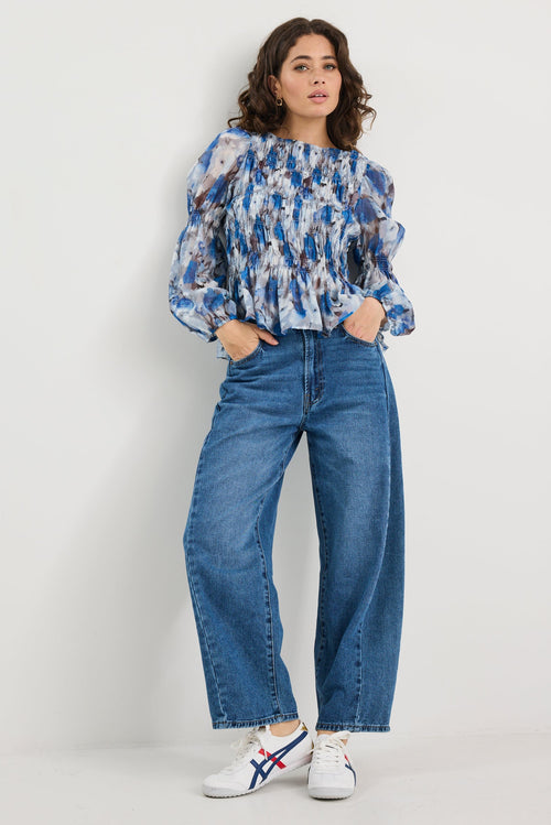 Woman wearing a blue patterned blouse and jeans on a white background