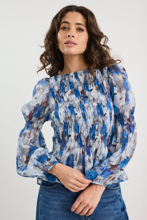 Woman wearing a blue and gray patterned blouse with jeans on a white background