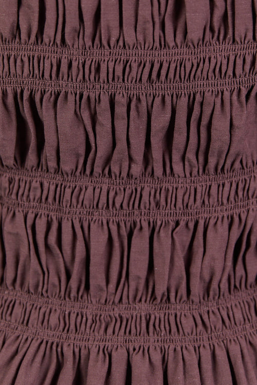 Close-up of a maroon dress with smocked waist and long sleeves.