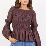 Woman wearing a brown smocked blouse and blue jeans on a white background