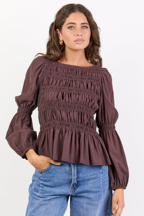 Woman wearing a brown smocked blouse and blue jeans on a white background