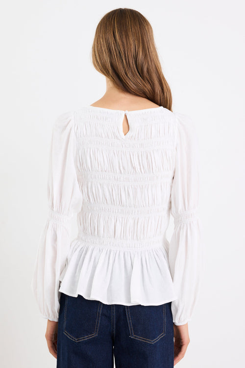 Woman wearing a white blouse with a peplum waist and blue jeans on a white background