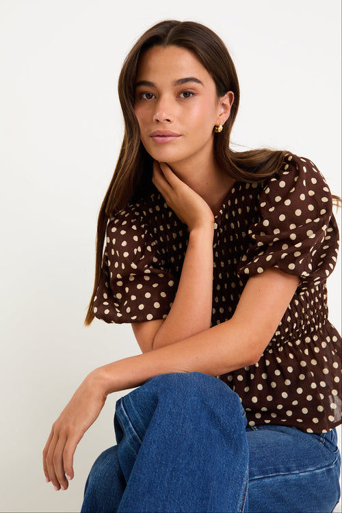 Model wearing a chocolate brown polka dot short sleeve top with a shirred bodice and peplum hem