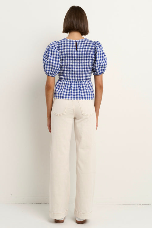 model wears a blue gingham puff sleeve top with ecru jeans