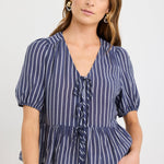 Woman wearing a navy and ivory striped short sleeve peplum top with tie-front closure, styled with ecru jeans.