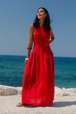 Woman in a red dress standing on a rocky beach with clear blue sky and ocean.