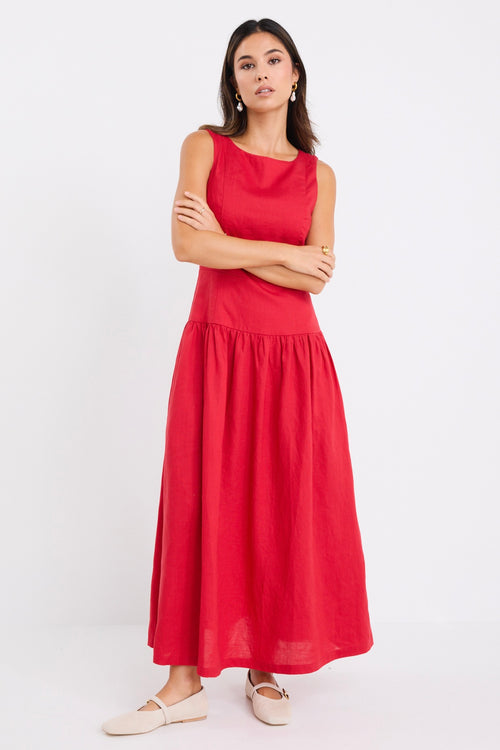 Woman wearing a sleeveless cherry red midi dress with a fitted bodice and gathered skirt, paired with neutral flats.