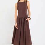 Woman wearing a chocolate brown sleeveless maxi dress with a structured bodice and flowing skirt, styled with black flat shoes