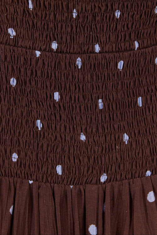 Close-up of a brown smocked fabric with small white polka dots, showing the texture and pattern detail.