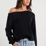 Woman wearing a black off-shoulder top and light blue jeans on a white background