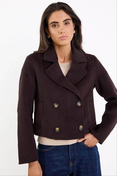Woman wearing a dark brown peacoat with gold buttons on a white background