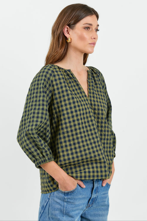 Woman wearing a green and black checkered blouse with blue jeans on a white background