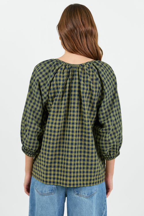 Back of a Woman wearing a green and black checkered blouse with blue jeans on a white background