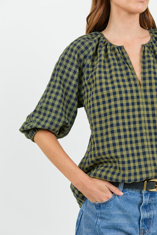Close up of a woman wearing a green and navy check blouse and blue jeans on a white background.