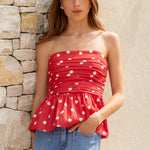 Woman wearing a red polka dot top and blue jeans against a stone wall.