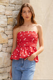 Woman wearing a red polka dot top and blue jeans against a stone wall.