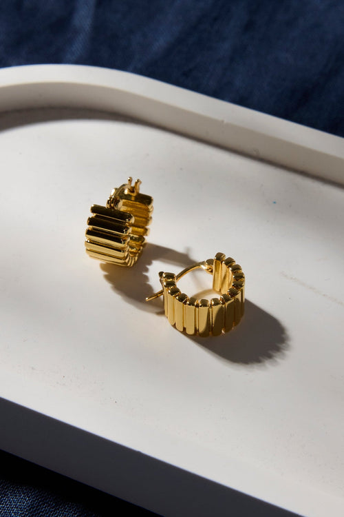 Gold hoop earrings on a white tray with a blue fabric background