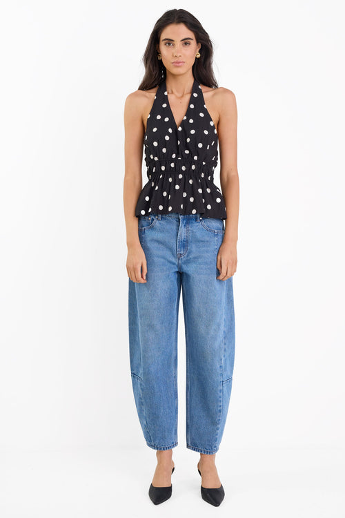 Woman wearing a black polka dot top and blue jeans on a white background
