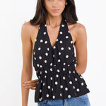 Woman wearing a black halter top with white polka dots and blue jeans on a white background