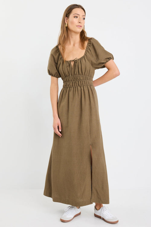 Woman wearing a khaki short sleeve linen blend midi dress with a shirred waist, tie neckline, and side split, styled with white sneakers.