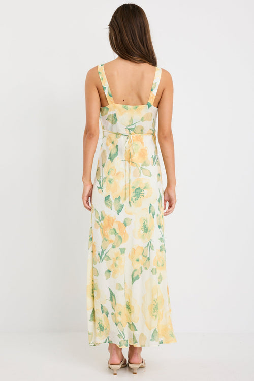 Woman wearing a strappy maxi dress with a honey-yellow floral print on a soft crinkle-textured fabric, cut on the bias for a floaty and elegant silhouette.