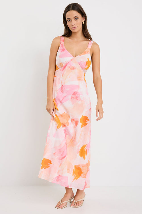 Woman wearing a strappy maxi dress with an abstract pink and orange sunset print, cut on the bias for a floaty and feminine silhouette.