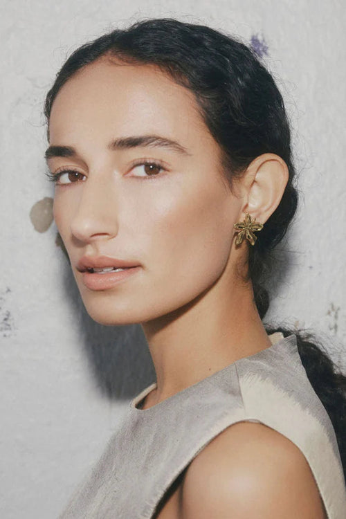 Woman wearing a gold earring against a neutral background